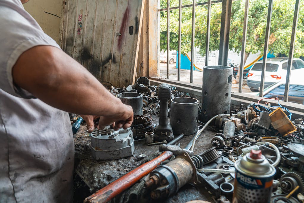 Imagen actual: Mechanic organizing auto parts in a busy workshop, surrounded by tools and equipment.