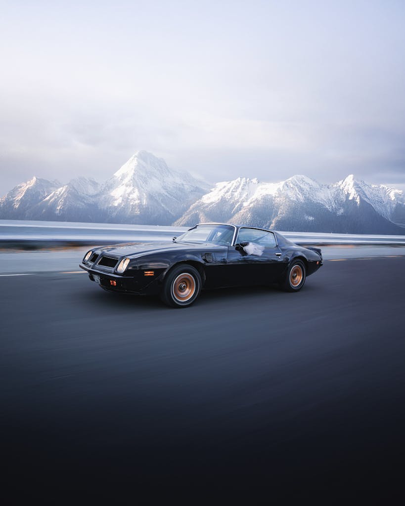 Imagen actual: A vintage sports car speeds along a road with stunning snowy mountains in the background, exuding adventure