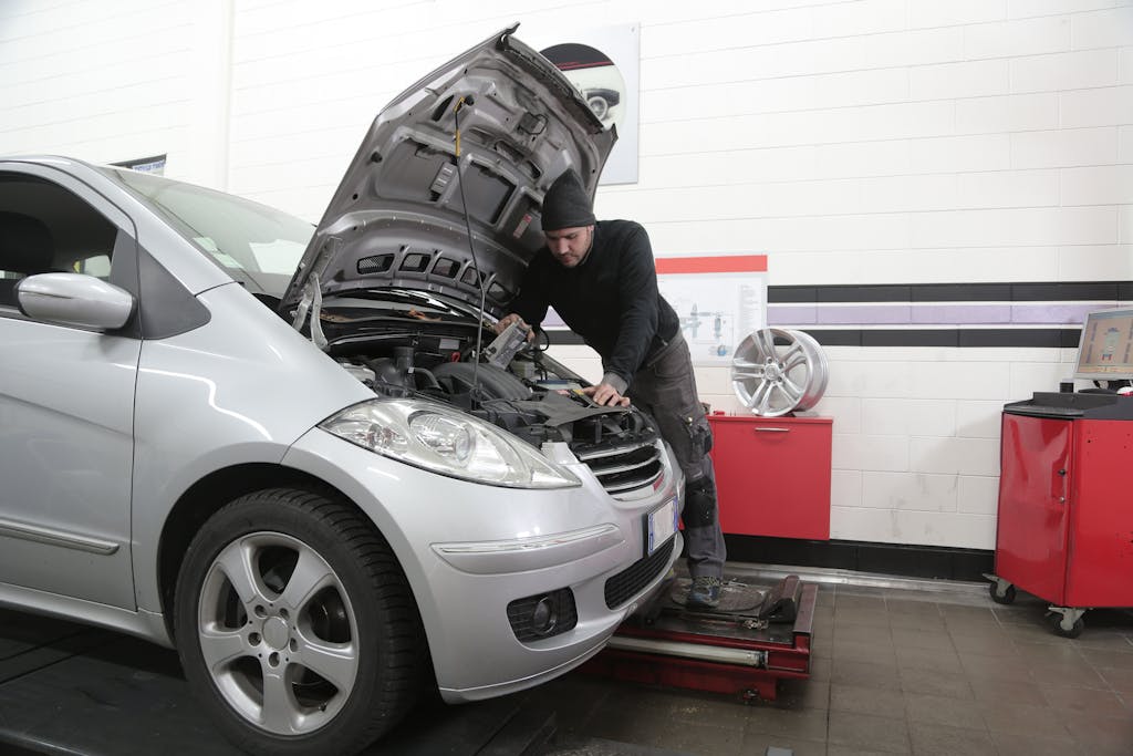 Imagen actual: A mechanic checks a car engine for maintenance in a garage setting.