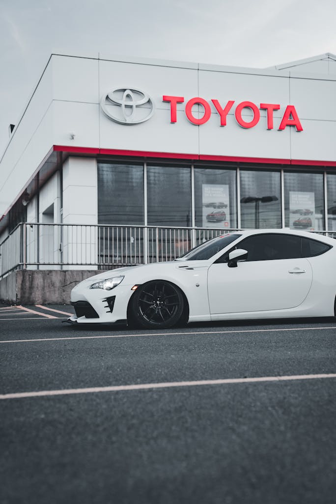 Imagen actual: A sleek white car is parked outside a Toyota dealership on a cloudy day.