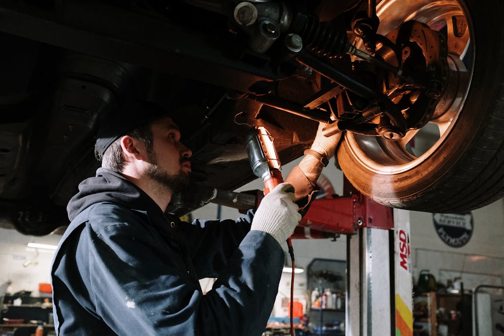 Imagen actual: Mechanic examining car's undercarriage at a garage, focusing on vehicle maintenance.