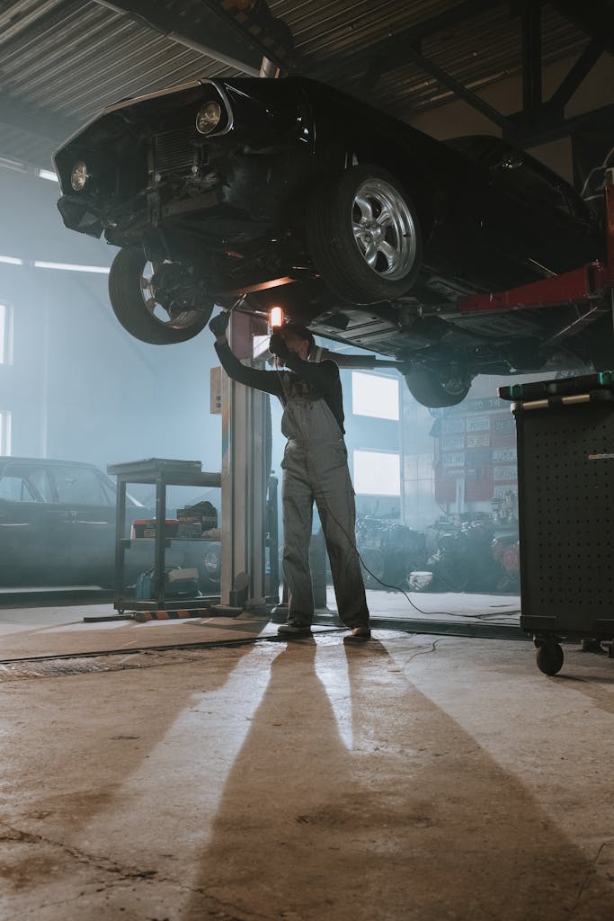 Imagen actual: Mechanic performing maintenance on elevated car in dimly lit garage, showcasing automotive repair work.