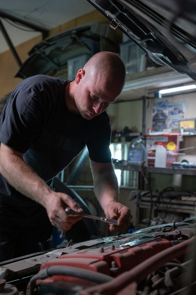Imagen actual: A mechanic is diligently working inside a garage, fixing a car engine under the hood.