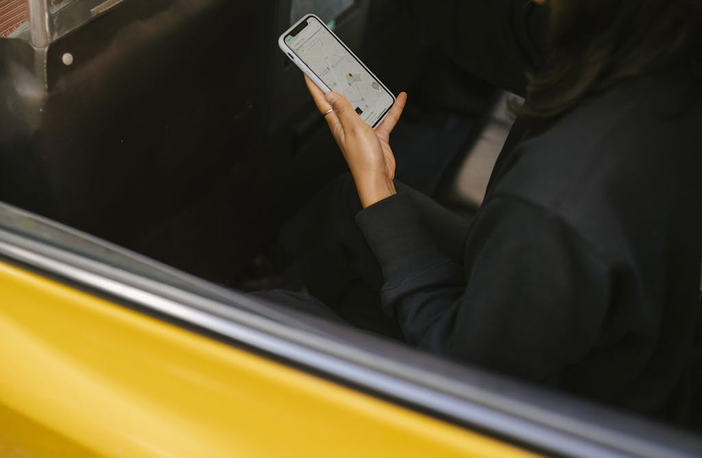 Imagen actual: A woman using a smartphone for navigation in a yellow taxi. Perfect for travel and technology themes.