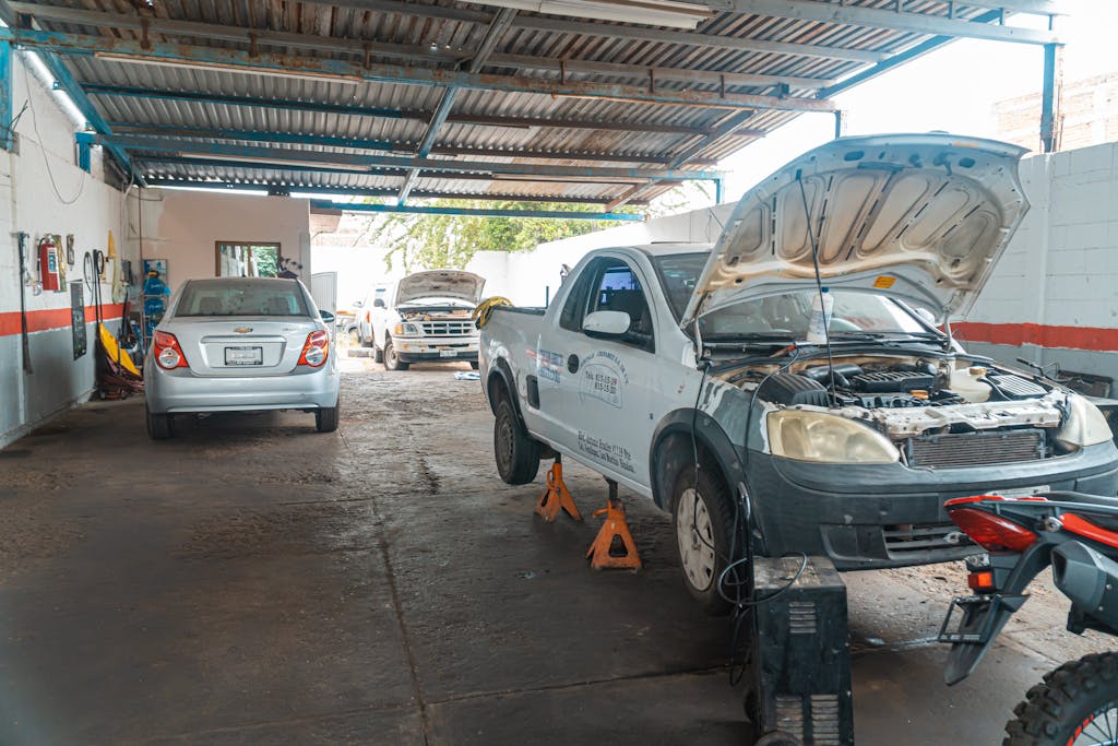 Imagen actual: Indoor car repair garage with multiple vehicles under maintenance, showcasing a bustling automotive environment.
