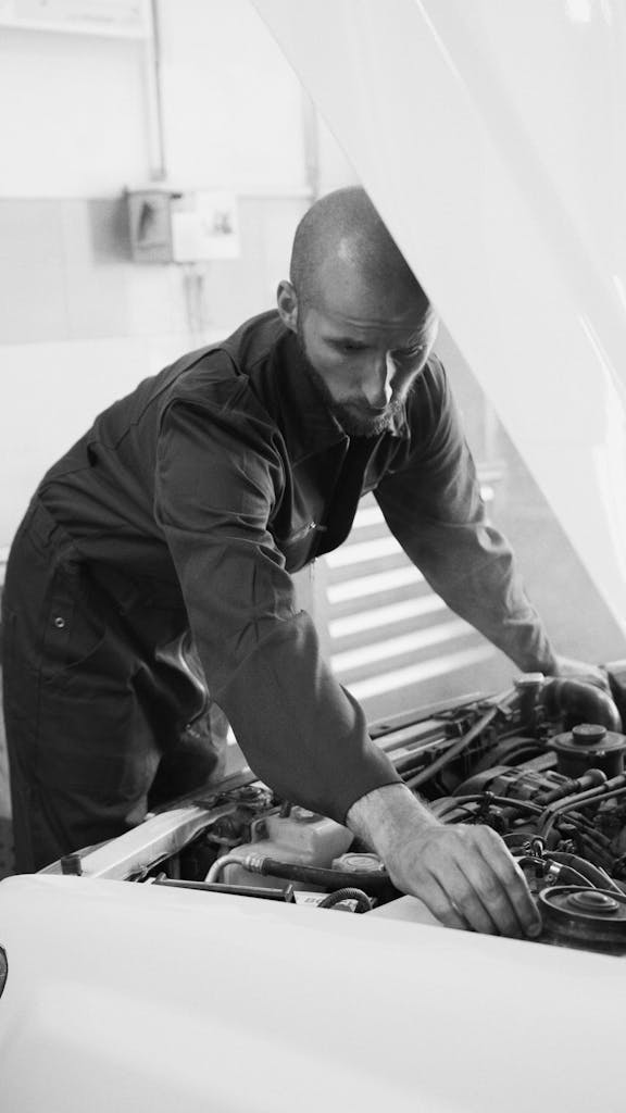 Imagen actual: Male mechanic working under a car hood in a workshop, focusing on engine repair.