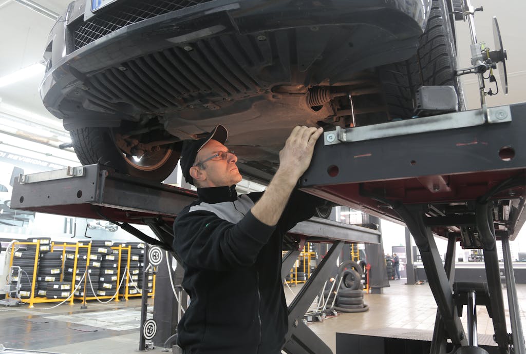 Imagen actual: Mechanic inspecting car on lift in an automotive garage, focusing on vehicle repair and maintenance.